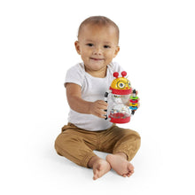 Baby activity rattle with yellow face and clear shaker tube, held by baby
