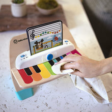 Adult hands pressing keys on wooden touch piano toy with attached screen