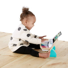 Baby playing wooden touch piano toy with tablet-style screen on tabletop