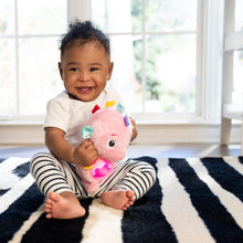 Baby holding pink seahorse plush soother with glowing belly and dangling tags