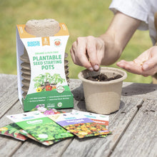 Plantable seed starting pots box beside a soil-filled pot and seed packets