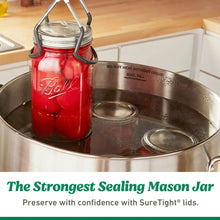 Mason jar in simmering canner with water and metal lid ring