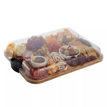 Bamboo cutting board with cheese knives holding cured meats, crackers, and small dips