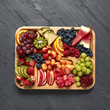 Bamboo cutting board holding mixed fruit slices and berries