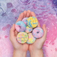 Hands holding round pastel bath bombs in blue, pink, purple, and yellow colors