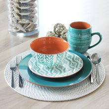 Turquoise dinnerware set on a woven placemat with teal mugs and patterned bowls.