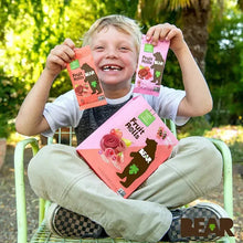 Fruit roll snack packs held by a smiling child outdoors