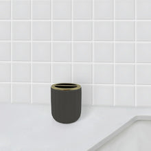 Grey cylindrical toothbrush holder with gold-toned rim on bathroom counter