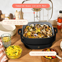 Black electric skillet with glass lid propped upright, cooking seafood