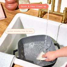 Detached black skillet pan being rinsed and scrubbed in a sink