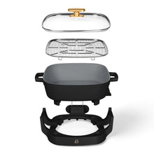 Exploded view of black electric skillet with glass lid, steaming tray, pan, and detachable base