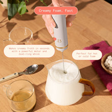 Taupe handheld milk frother whisking milk in a glass pitcher