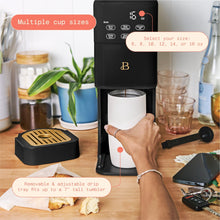 Black single-serve coffee maker shown brewing into a tall travel tumbler; removable drip tray