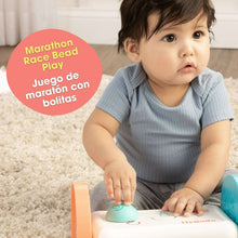 Baby using activity mirror base, blue outfit beside orange-and-teal toy