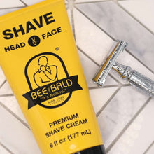 Bee Bald premium shaving cream tube close-up, yellow/black, head & face, next to razor
