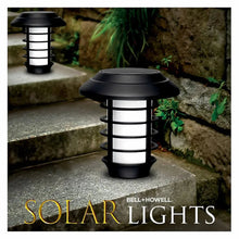 Black solar pathway stake light with lantern top and glowing light, outdoor stone steps.