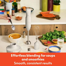 Immersion blender with whisk attachment and blending cup on a kitchen counter