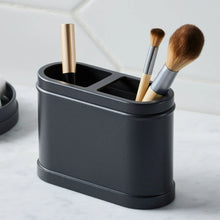 Black metal toothbrush holder with three openings holding brushes