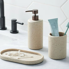Speckled beige toothbrush holder with toothbrushes standing in the open cup