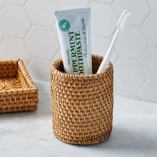 Woven rattan toothbrush holder holding a toothbrush and toothpaste tube, open top