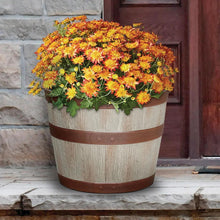 Whiskey barrel-style resin planter holding yellow-orange flower arrangement, light brown and white woodgrain
