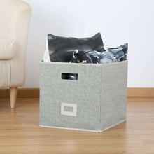 Gray fabric cube storage bin with cutout handles, filled with folded items