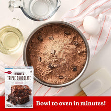 Bowl of brownie mix powder with oil, eggs, and a triple chocolate mix box