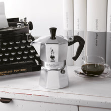 Silver stovetop espresso maker with black handle and knob, placed on countertop