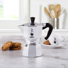 Silver stovetop espresso maker with black handle and knob, front view on counter