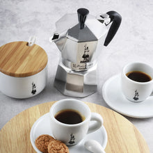 Silver stovetop espresso maker with black knob and handle, angled front view