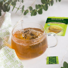 Glass cup of brewed green tea with steeping stream and tea bag box