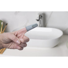 Baby silicone finger toothbrush held over sink, gray brush with textured bristles