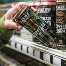 Hand holding a Black Rifle Coffee Company Espresso Mocha can beside other cans