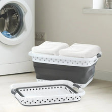 Collapsible laundry basket holding folded towels, gray with white perforated rim