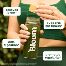 Bloom greens & superfoods powder jar held by hands with green drink