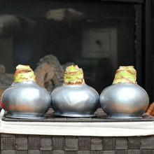 Waxed amaryllis trio with silver bulb bases and green wax caps, set on a mantle.