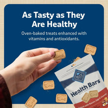 Hand holding Health Bars dog biscuit with more biscuits and treat bag shown