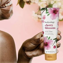 Bodycology cherry blossom body cream tube held in hand with pink floral artwork and gold cap