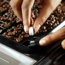 Hands scrubbing dark coffee grounds with a small cleaning brush on an espresso part.