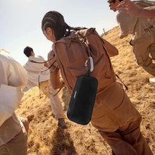 Black portable Bluetooth speaker hanging from a backpack with carry strap