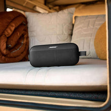 Black portable Bluetooth speaker on a couch seat, with grille and carry strap