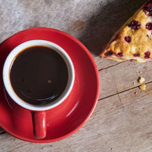 Red mug filled with dark roast coffee on a wooden surface