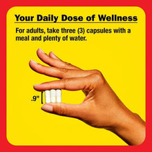 Hand holding three white capsules over a yellow wellness dosing card