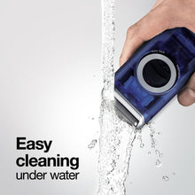 Blue electric shaver held in hand with foil head aimed at water stream.