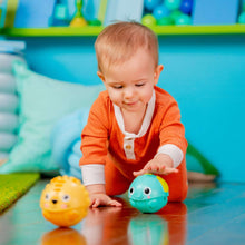 Baby reaching for a teal rolling animal ball with a yellow lion ball nearby