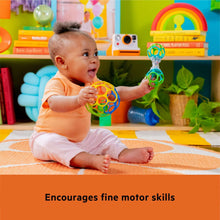 Baby sitting holding a colorful ring rattle ball with dangling bead pieces