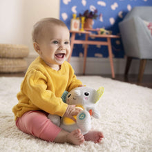 Baby playing with a gray plush elephant soother on a rug