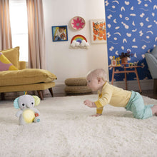 Gray plush elephant soother on rug while a toddler reaches toward the toy