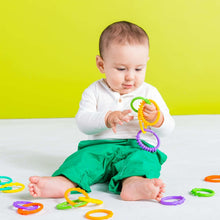 Infant holding colorful link loop rings while lying on green pants, with purple and orange rings