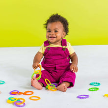 Baby playing with colorful interlocking loop link rings on the floor, including green and yellow